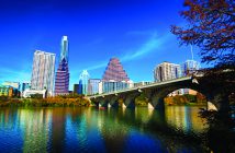 Austin downtown skyline with a bridge, Lady Bird / Town Lake, and an Autumn colored tree.