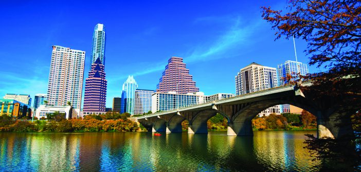Austin downtown skyline with a bridge, Lady Bird / Town Lake, and an Autumn colored tree.