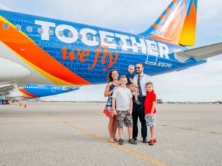 A pilot stands with his family in front of an Allegiant plane with a new livery that reads "Together We Fly".